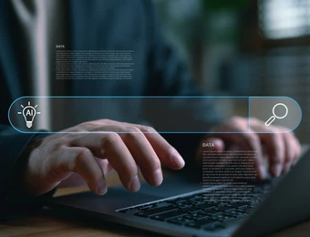 Nahaufnahme: Hände tippen auf einem Laptop; eine blaue holografische UI schwebt darüber.