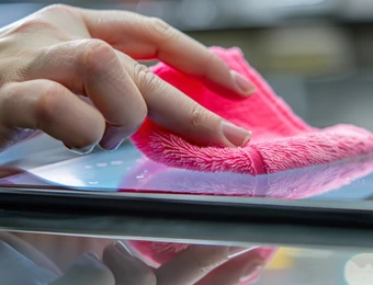 Nahaufnahme einer Hand, die ein pinkes Mikrofaser-Tuch über eine glatte Glasoberfläche wischt.