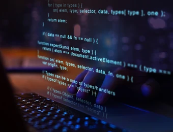 Dunkler Bildschirm mit blau leuchtendem Code, tippende Hände über einer Laptop-Tastatur.