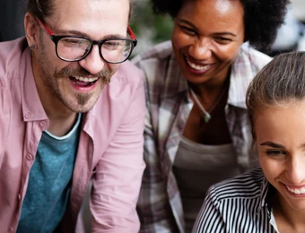 Drei Personen schauen gemeinsam auf eine Fläche und lächeln.