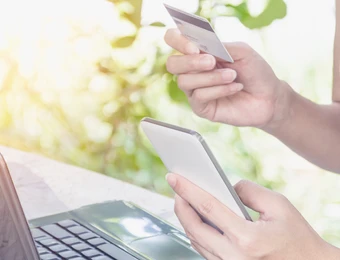 Laptop auf einem Tisch; rechts hält eine Person im gestreiften Oberteil ein Smartphone.