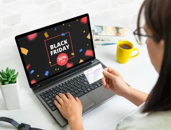 Person nutzt Laptop; Bildschirm zeigt Black Friday 30% Off. Hand hält Kreditkarte; gelbe Tasse, Pflanze auf weißem Tisch.