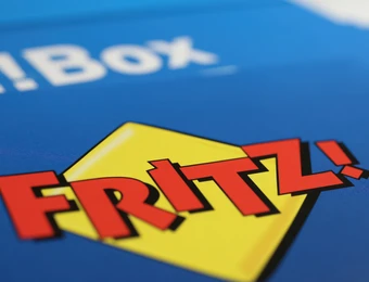 Nahaufnahme des FRITZ!-Logos: roter Schriftzug auf gelbem Quadrat, vor blauem Hintergrund.