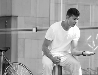 Zwei Männer in weißen T-Shirts vor einer Glasfassade; ein Fahrrad steht an einer Stange daneben.