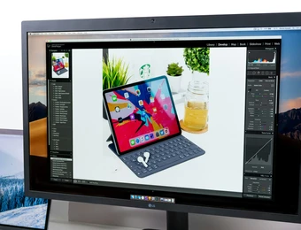 Monitor zeigt eine bearbeitete Fotoaufnahme eines Tablets mit Tastaturhülle; Hintergrund mit Pflanzen und Glasgefäß.
