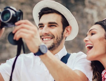 Zwei Personen im Freien; ein Mann mit weißem Hut fotografiert, daneben lächelnde Frau.