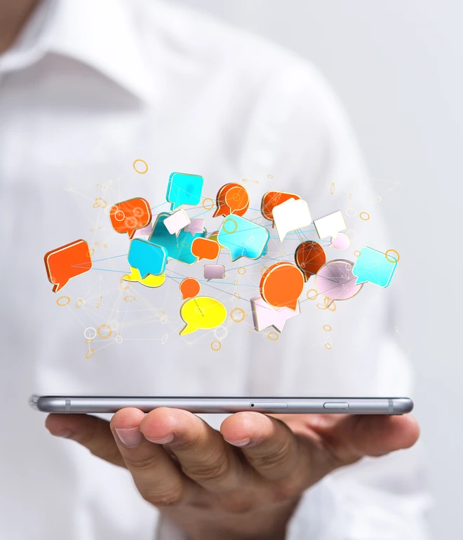 Hände halten ein Smartphone; bunte Sprechblasen steigen aus dem Bildschirm.