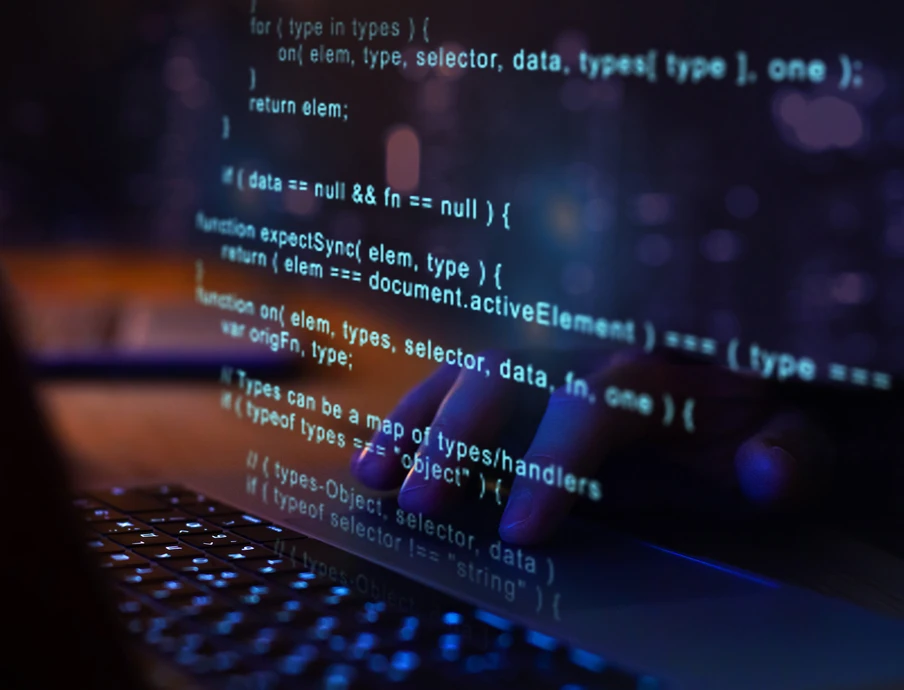 Dunkler Bildschirm mit blau leuchtendem Code, tippende Hände über einer Laptop-Tastatur.