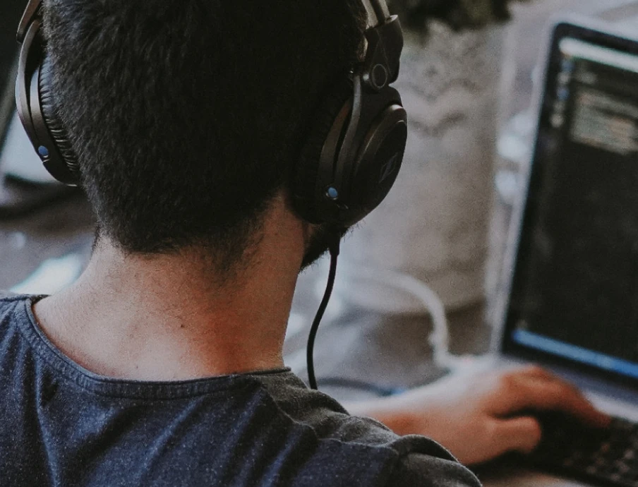 Person von hinten sitzend, mit Headset, vor zwei Laptops; Bildschirm zeigt Code.