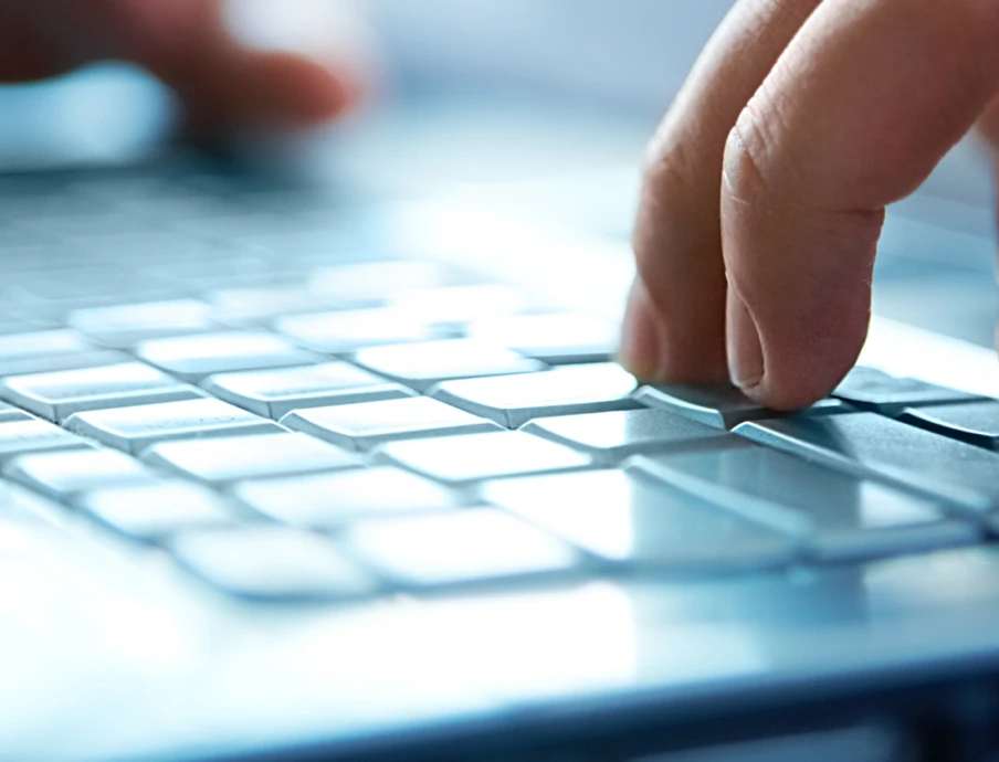 Nahaufnahme: Hände tippen auf einer Laptop-Tastatur; silbernes Gehäuse, helle Tastenbeleuchtung.