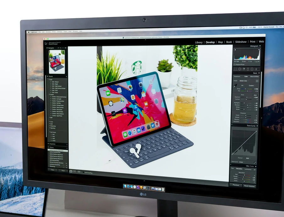 Monitor zeigt eine bearbeitete Fotoaufnahme eines Tablets mit Tastaturhülle; Hintergrund mit Pflanzen und Glasgefäß.