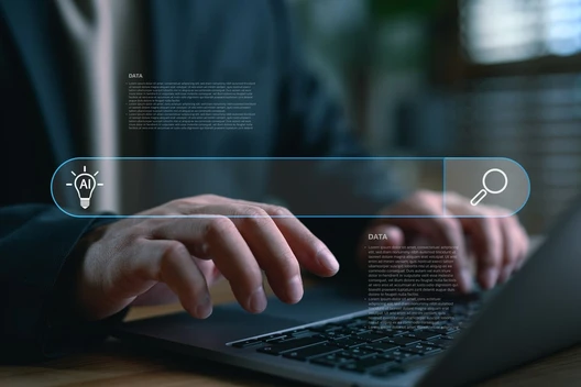 Nahaufnahme: Hände tippen auf einem Laptop; eine blaue holografische UI schwebt darüber.