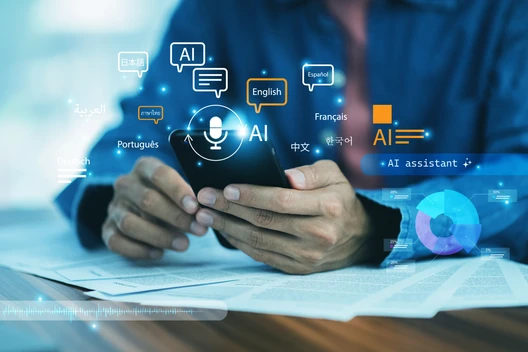 Person hält Smartphone; holografische AI-Icons, Sprachen-Symbole, Diagramme über einem Tisch mit Papieren.