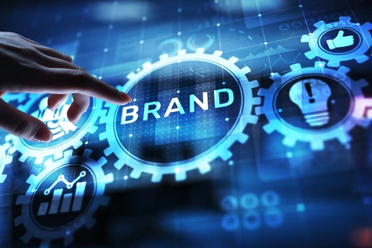 Eine Hand berührt eine leuchtende Scheibe mit dem Wort BRAND, umgeben von blauen Zahnrädern und Symbolen.